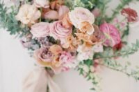 a delicate wedding bouquet of pink, light pink and fuchsia ranunculus, rust sweet peas and greenery and long grey ribbons