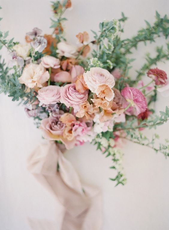 a delicate wedding bouquet of pink, light pink and fuchsia ranunculus, rust sweet peas and greenery and long grey ribbons