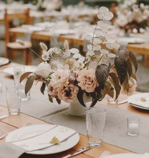 a delicate wedding centerpiece of blush carnations, dark leaves, white roses and bunny tails plus lunaria is chic and lovely
