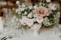 a delicate wedding centerpiece of blush, white and dusty pink blooms including roses and sweet peas and greenery for a refined wedding