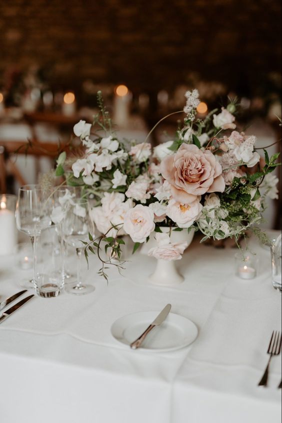 a delicate wedding centerpiece of blush, white and dusty pink blooms including roses and sweet peas and greenery for a refined wedding