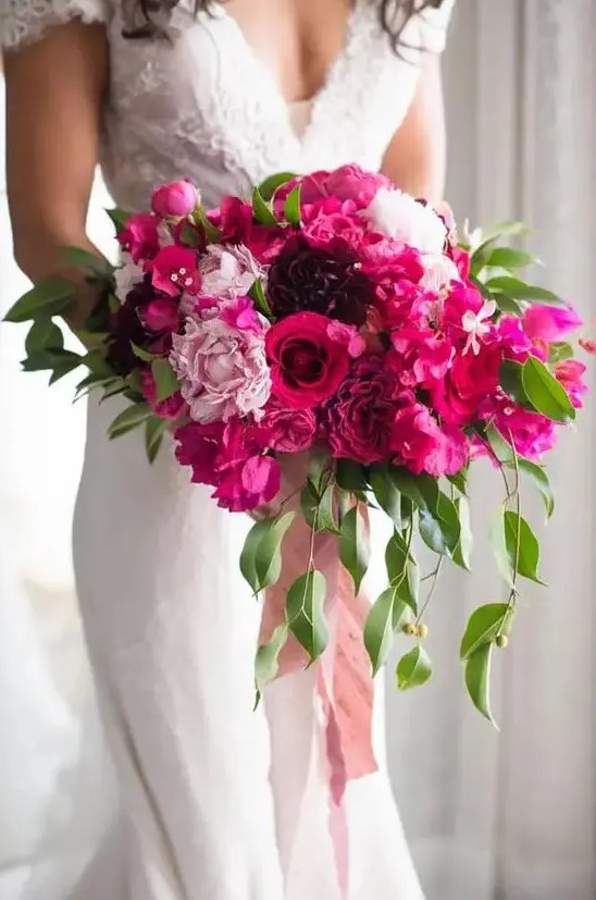 a dimensional and luxurious wedding bouquet of light pink, fuchsia and purple blooms, greenery and pink ribbon is amazing