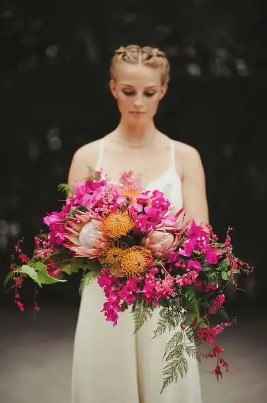a dimensional and textural cascading wedding bouquet of fuchsia blooms, pincushion proteas, king proteas, greenery and leaves for a bold wedding
