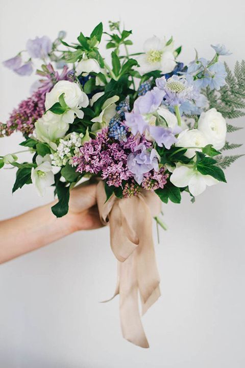 a dimensional and textural wedding bouquet of white ranunculus, lilac, blue and lilac sweet peas, some bulbs and greenery