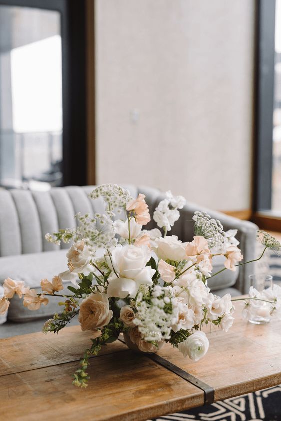a dimensional wedding centerpiece of white roses and ranunculus, coffee-colored blooms, sweet peas and some fillers for spring or summer