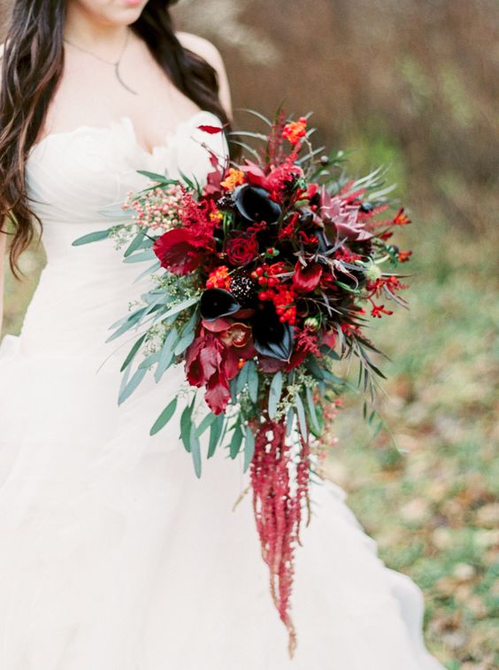 a dramatic wedding bouquet of red and black calla lilies, red berries, greenery and bold foliage, some amaranthus for a Halloween wedding