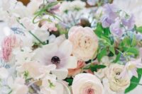 a dreamy spring wedding centerpiece of white and pink ranunculus, lilac sweet peas, greenery and some other blooms