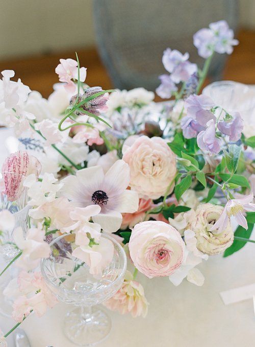 a dreamy spring wedding centerpiece of white and pink ranunculus, lilac sweet peas, greenery and some other blooms