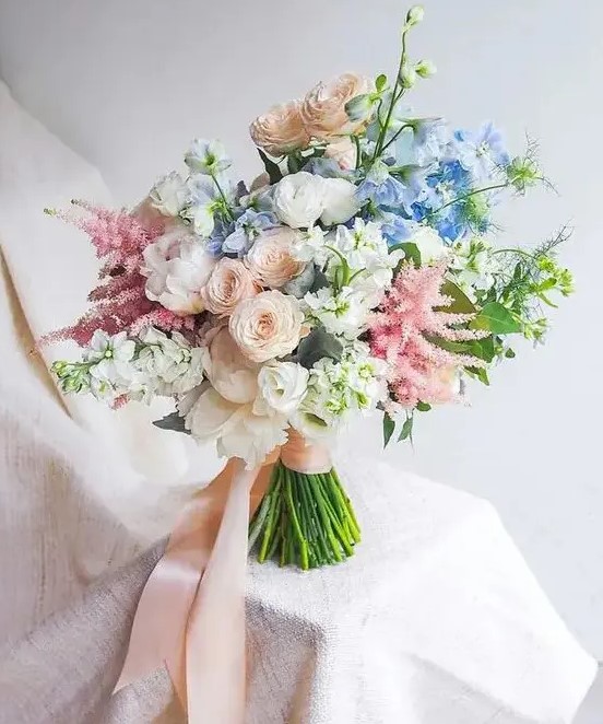 a dreamy wedding bouquet of white peonies, blush and white ranunculus, astilbe, blue blooms and blush ribbons for a garden bride
