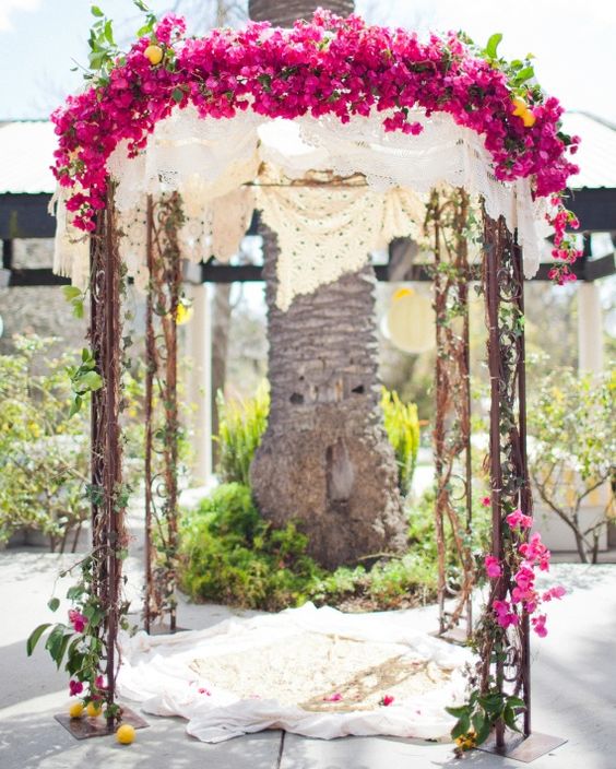 a fairy-tale wedding arch covered with doilies, bougainvillea and greenery plus a rug is a bold and lovely idea for a summer wedding