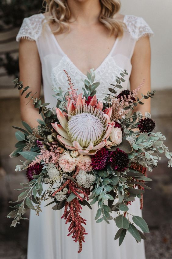 a fall wedding bouquet of blush and burgundy blooms, a king protea, greenery, amaranthus is a stunning idea for the fall