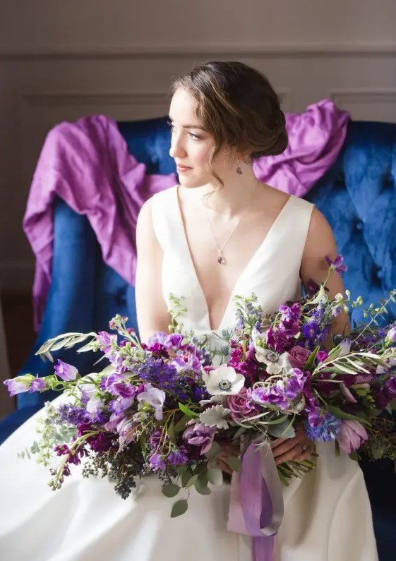 a fantastic purple wedding bouquet with pink and lilac blooms, white anemones and greenery and pale leaves plus grey and purple ribbon