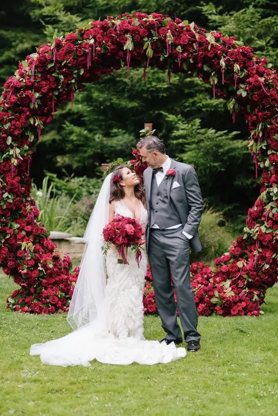 a fantastic round wedding arch covered with deep red and burgindu blooms and greenery for a bright fall wedding