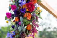 a fantastic wedding arch decorated with purple, violet, hot pink, red, orange and yellow blooms and greenery, with much texture