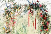 a fun and colorful wedding arch of white, blush, yellow, red, burgundy and blue flowers, greenery and garlands