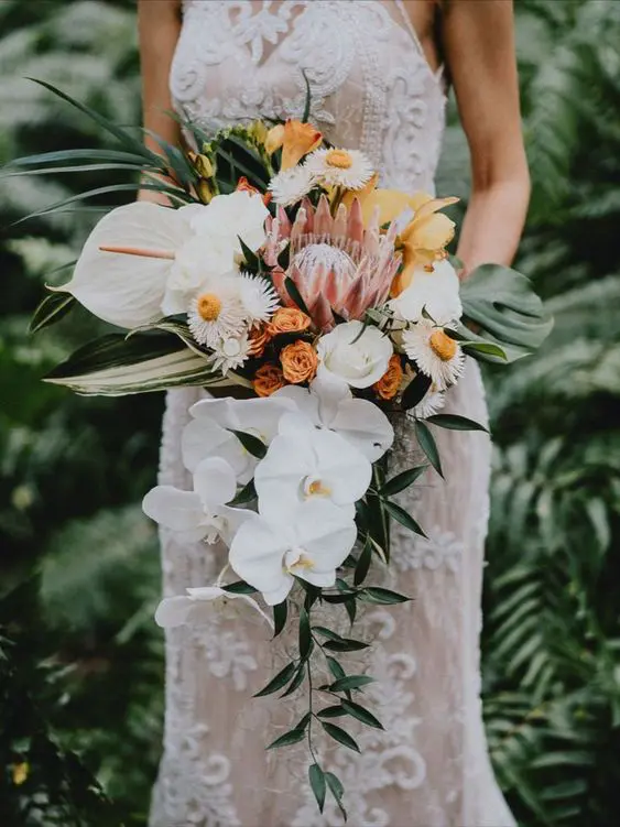 a gorgeous tropical wedding bouquet of white orchids, white roses and daisies, yellow blooms, a king protea and anthurium and greenery