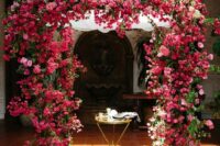a jaw-dropping lush wedding arch covered with bougainvillea and pink peonies and roses plus some leaves is gorgeous