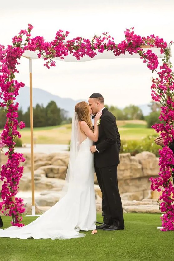 a jewel-tone wedding arch covered with magenta blooms and greenery is a lovely color statement to rock