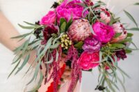 a jewel-tone wedding bouquet of hot pink and fuchsia blooms, king protea, greenery, berries and amaranthus plus long colorful ribbons