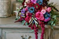a jewel-tone wedding bouquet of pink and fuchsia blooms, some blue thistles, purple touches, greenery and amaranthus for a fall wedding