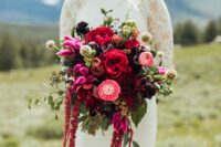 a jewel-tone wedding bouquet of pink, red and burgundy blooms including ranunculus, peonies, amaranthus and some greenery and seed pods