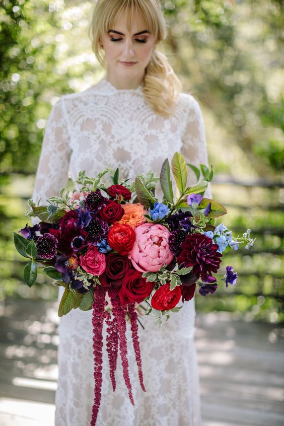a jewel-tone wedding bouquet of red roses, purple and burgundy blooms, orange and blue ones, greenery and amaranthus for a colorful wedding