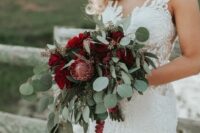 a laconic fall wedding bouquet of burgundy roses and king proteas, greenery and amaranthus is amazing for a fall wedding