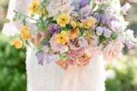 a lovely bright wedding bouquet of blush roses, yellow blooms, lilac blooms including sweet peas and greenery for spring or summer