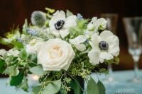 a lovely wedding centerpiece of white roses and anemones, greenery, blue blooms and allium plus eucalyptus and candle is a chic idea