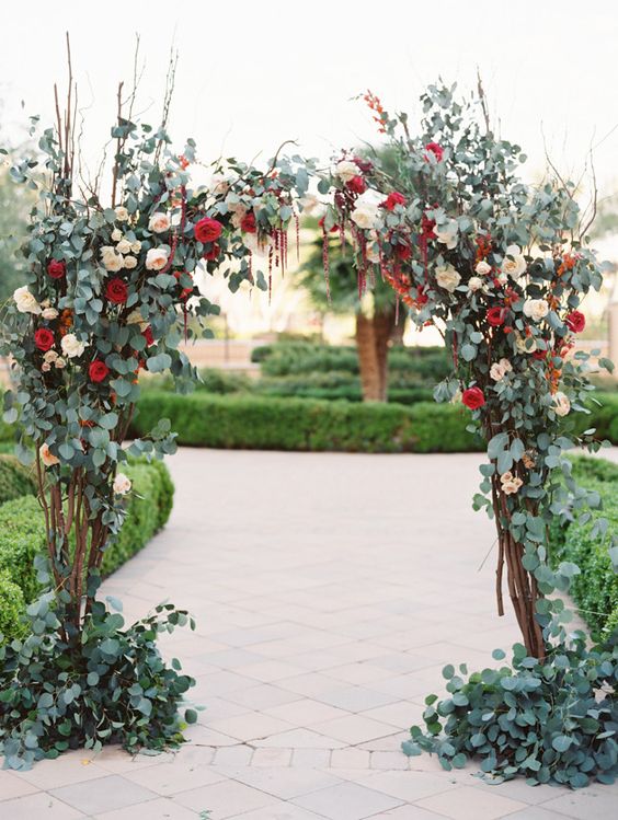 a lush and chic fall wedding arch with greenery, twigs and branches, blush and burgundy roses and amaranthus is wow