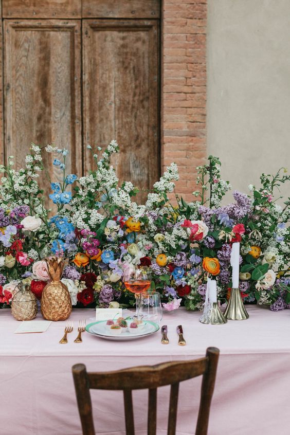 a lush and colorful wedding centerpiece of lilac, yellow and blush ranunculus, greenery, blue blooms and sweet peas for a summer wedding