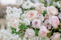 a lush and delicately colored wedding centerpiece of white sweet peas, blush peony roses, pale pink roses and orchids and geenery