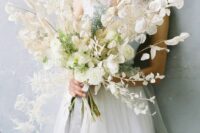 a lush and dimensional wedding bouquet of lunaria, some greenery and some dried leaves is an ethereal and airy arrangement for spring