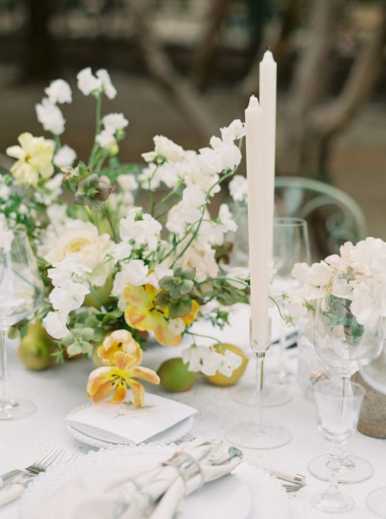a lush and dimensional wedding centerpiece of yellow tulips and white sweet peas plus fruit right on the table