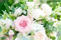 a lush and fresh centerpiece with white and pink roses, daisies and greenery in a gold bowl