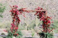 a lush wedding arch with bougainvillea, burgundy and red roses, ferns in pots on both sides of the arch