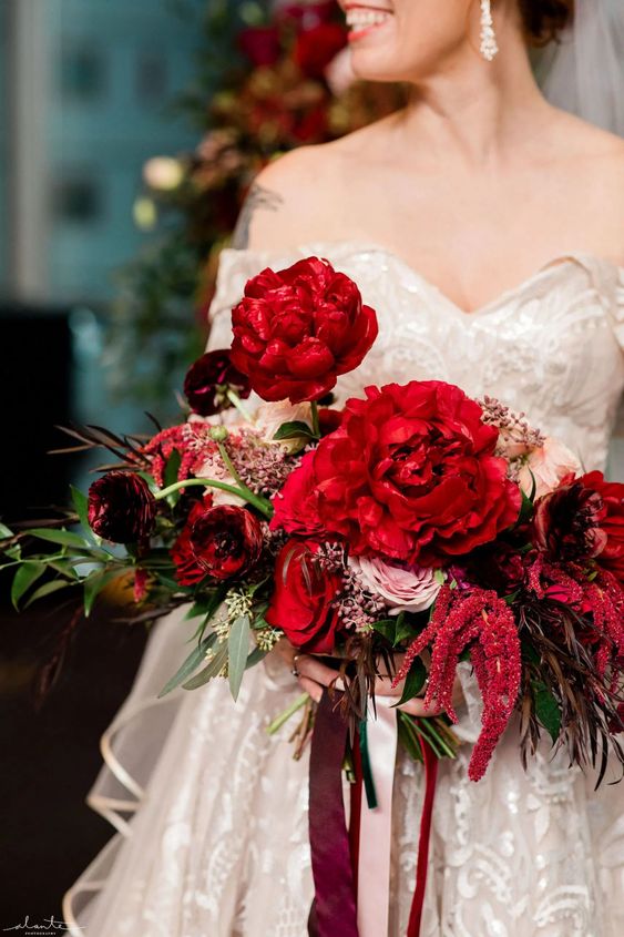 a luxurious wedding bouquet of red and pink roses and red peonies, greenery and amaranthus plus long ribbon
