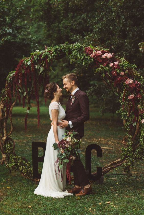 a moody round wedding arch of branches, with greenery, pink and burgundy blooms and amaranthus is a lovely idea for a fall wedding