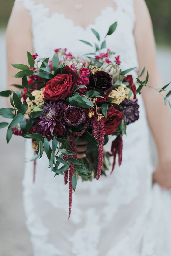 a moody wedding bouquet of burgundy roses, purple ranunculus and dahlias, greenery and amaranthus is amazing for the fall