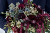 a moody wedding bouquet of deep burgundy roses and other blooms, waxflowers, thistles, greenery and amaranthus for fall or winter