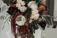 a moody wedding bouquet of white roses and ranunculus, king proteas, greenery and amaranthus plus thistles for the fall