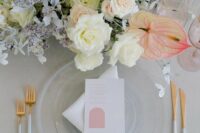 a neutral table setting with clear plates, gold and white cutlery, a neutral wedding centerpiece of white roses and anthurium