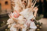 a neutral wedding bouquet of white orchids, king proteas, white anthurium, grasses and euclayptus is cool for a boho bride