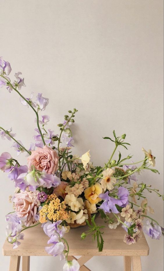 a pastel-colored wedding centerpice of yellow and peachy blooms, blush roses, lilac sweet peas is a refined and chic idea
