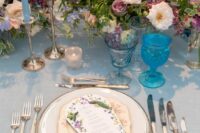 a pastel wedding centerpiece of lilac and blue sweet peas, white, mauve and lilac blooms and blue candles is adorable