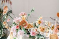 a pastel wedding centerpiece of pink carnations, yellow roses, anthurium, sweet peas and greenery plus seed pods