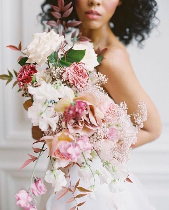 a pink cascading wedding bouquet of coffee-colored and white roses, pink carnations, pink sweet peas, some fillers and bold leaves