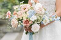 a pretty lush wedding bouquet of blush, white and mauve roses, white ranunculus, blue sweet peas and greenery for spring