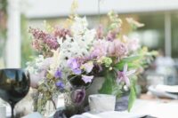 a purple wedding centerpiece of purple and white sweet peas, lilac and mauve roses and greenery for spring or summer