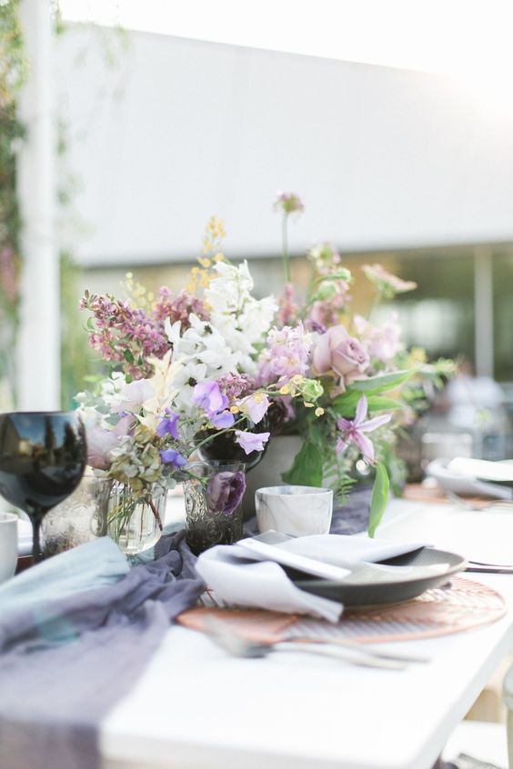 a purple wedding centerpiece of purple and white sweet peas, lilac and mauve roses and greenery for spring or summer